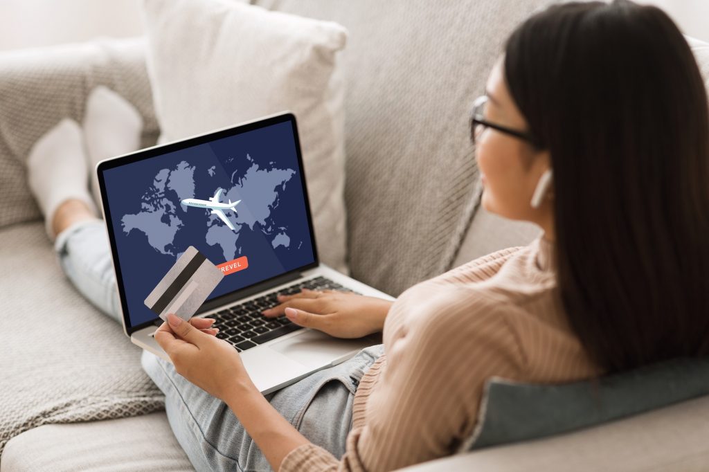 Airplane tickets and modern gadgets. Asian woman in glasses and wireless headphones sits on couch